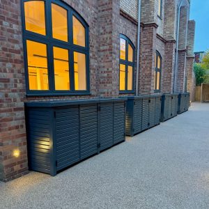 Quadruple wheelie bin storage unit alongside brick building